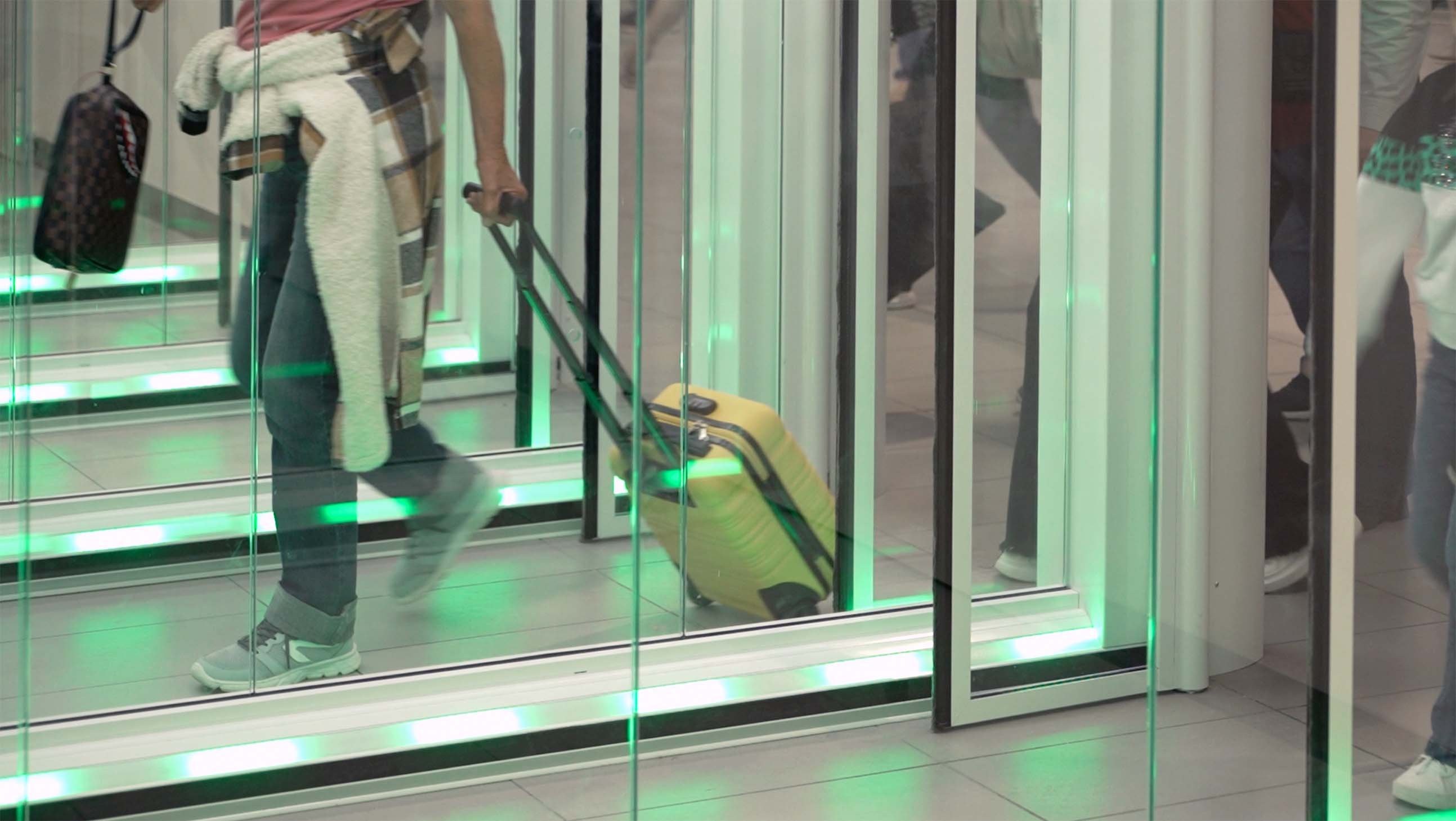 Passenger with a trolley case walking through a FAAC One-Way Corridor, with green LED signalling indicating the passage is available
